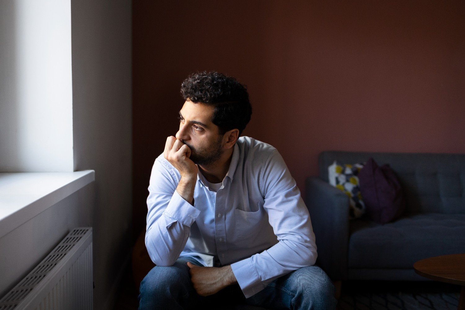 A man sitting alone and staring out the window with a thoughtful expression, symbolizing guilt in relationships and emotional reflection.